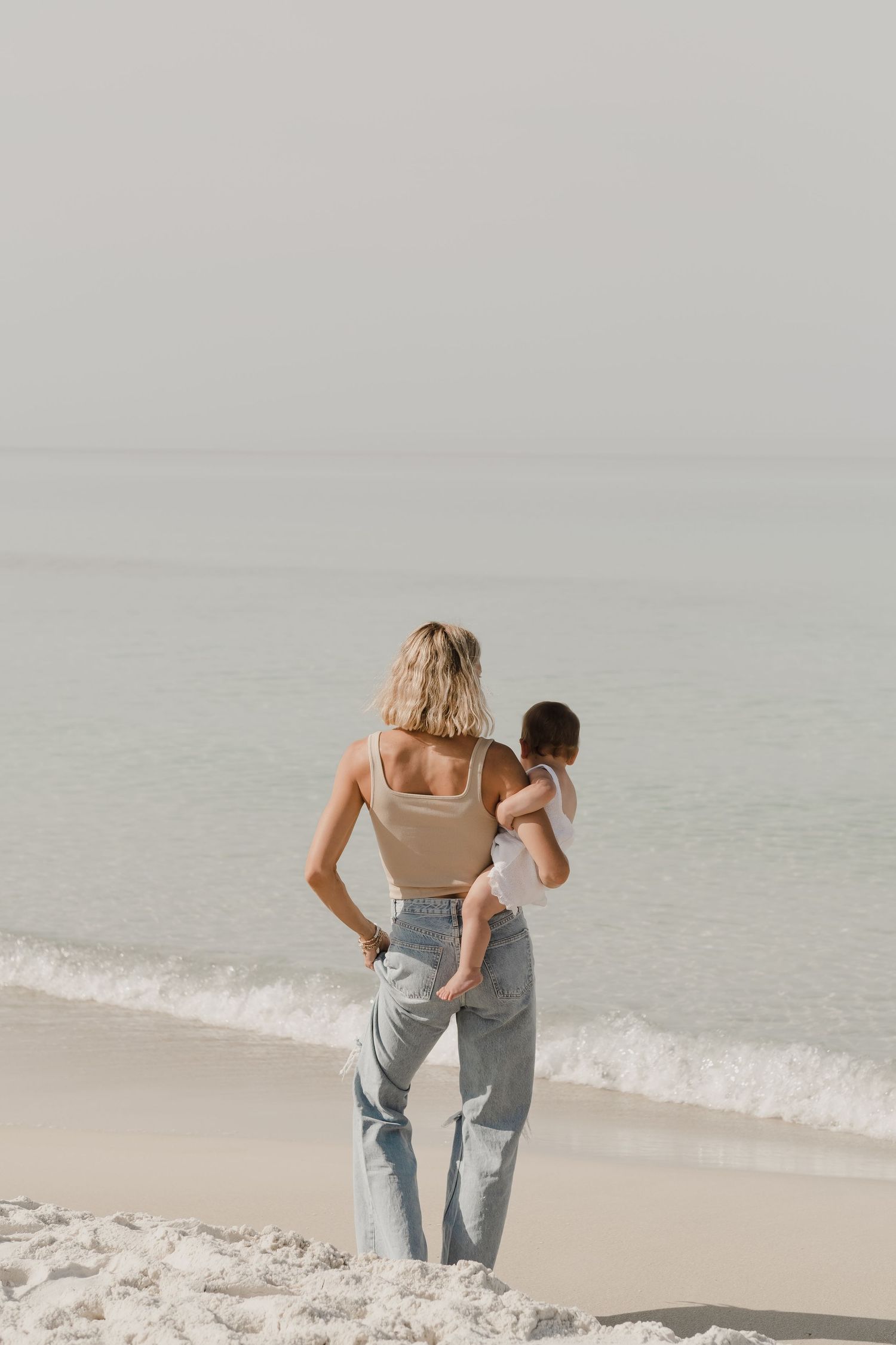 Couple walking together along a serene beach shoreline in casual attire.
