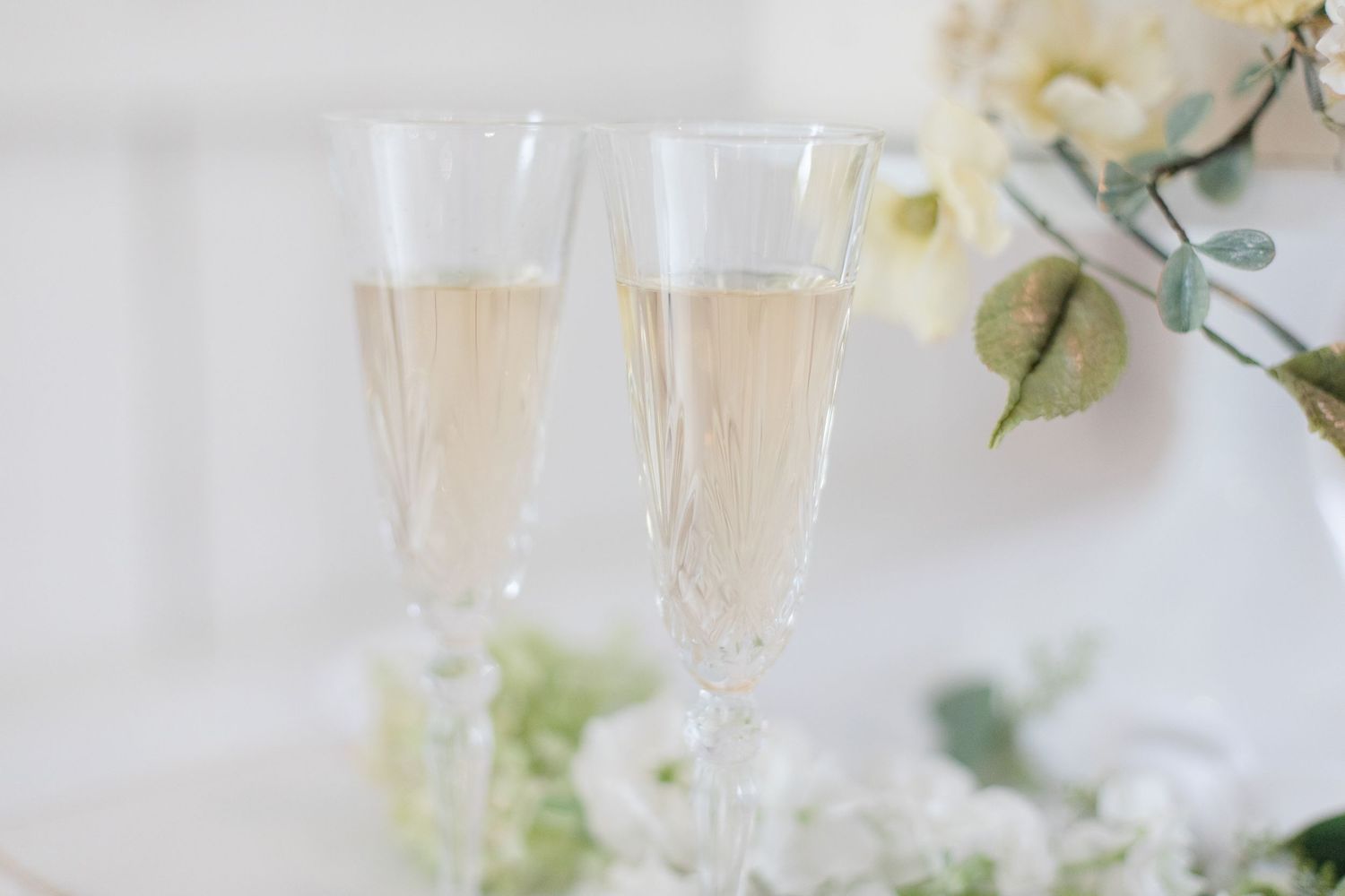 Champagne glasses and white floral decorations arranged on a rustic white surface.