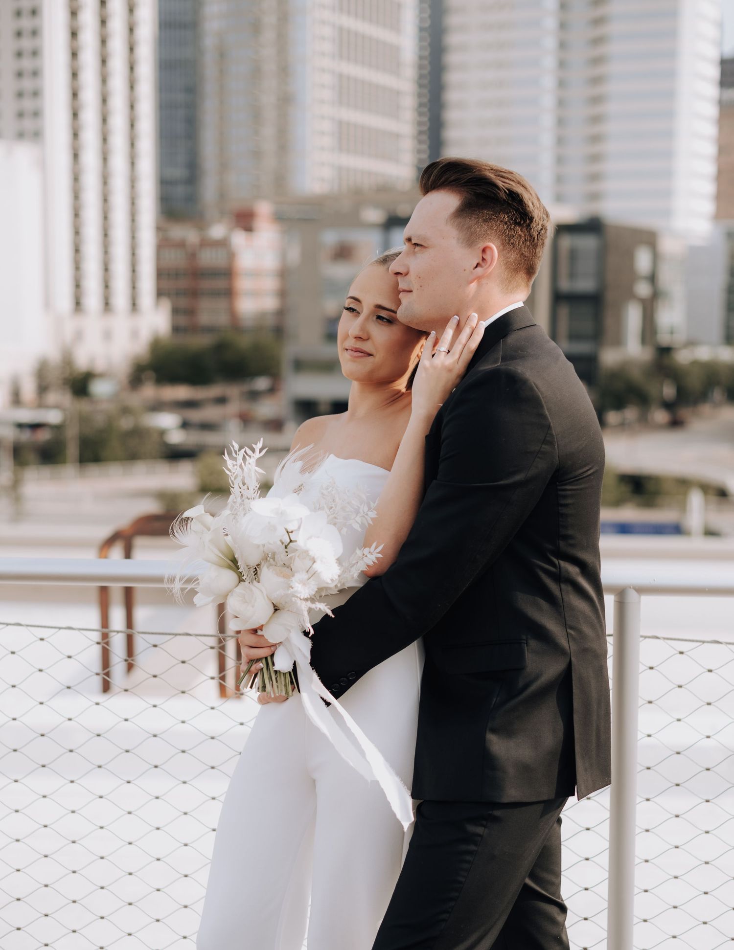 Elegant couple embracing during wedding photos with city backdrop.