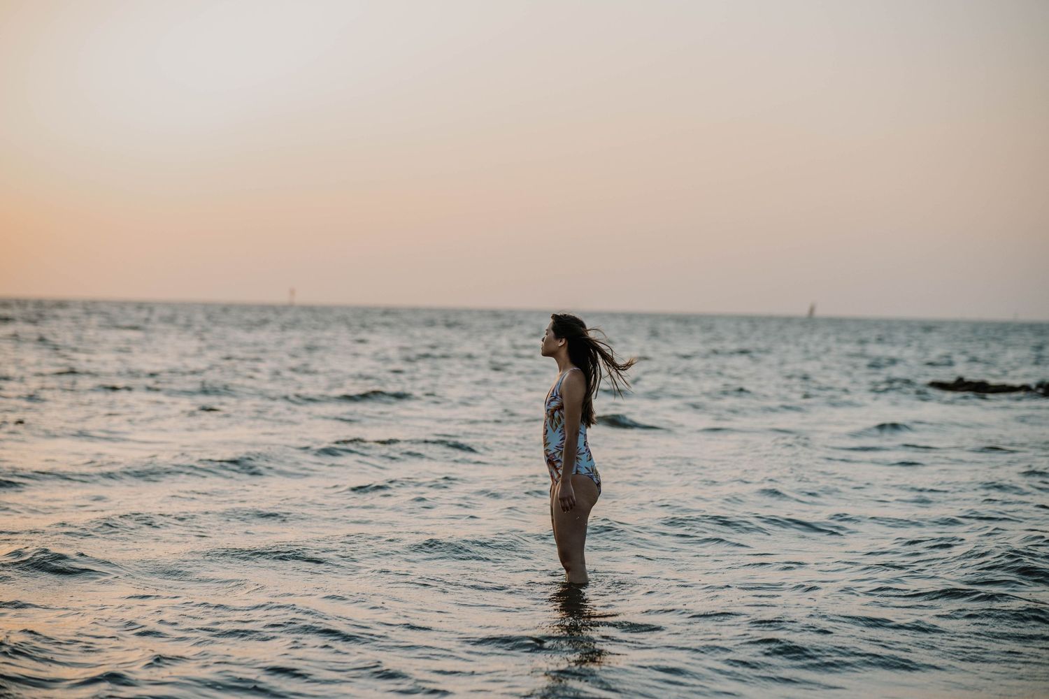Person standing in shallow ocean water during golden hour sunset.