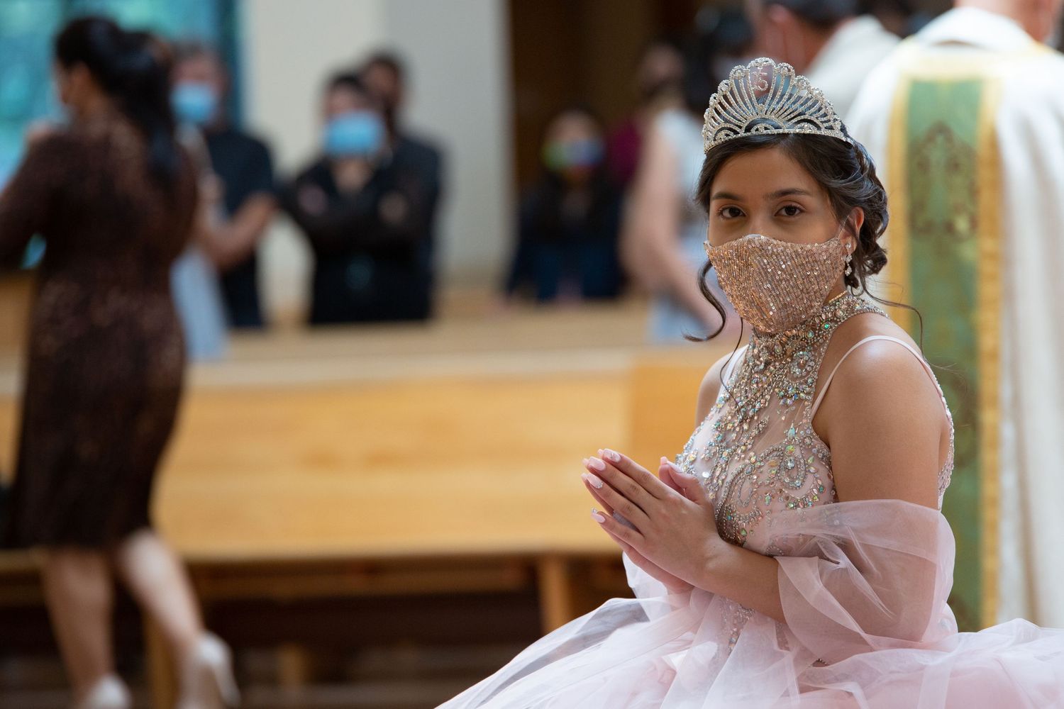 A person in a sparkly quinceañera dress and tiara wears a protective face mask during a celebration.