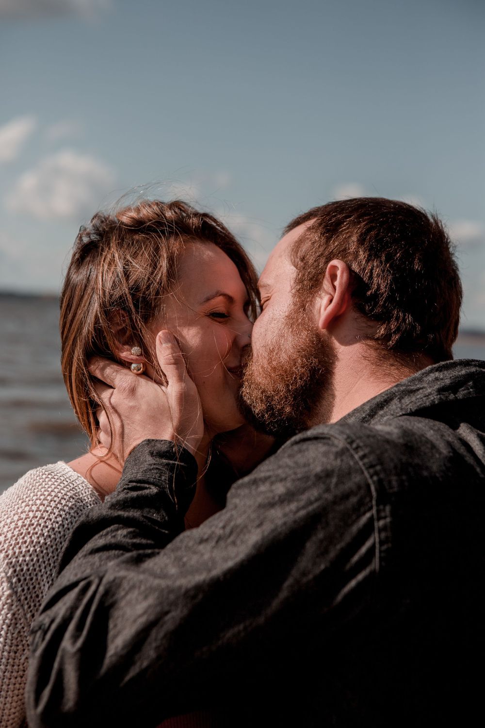 A tender moment between a couple sharing multiple kisses against a soft blue sky backdrop.