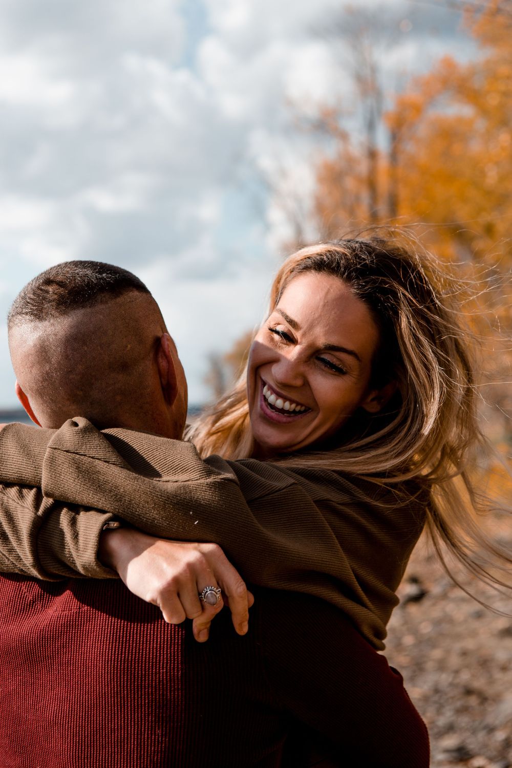 Joyful autumn engagement photos showing playful moments between a couple with fall foliage in the background.
