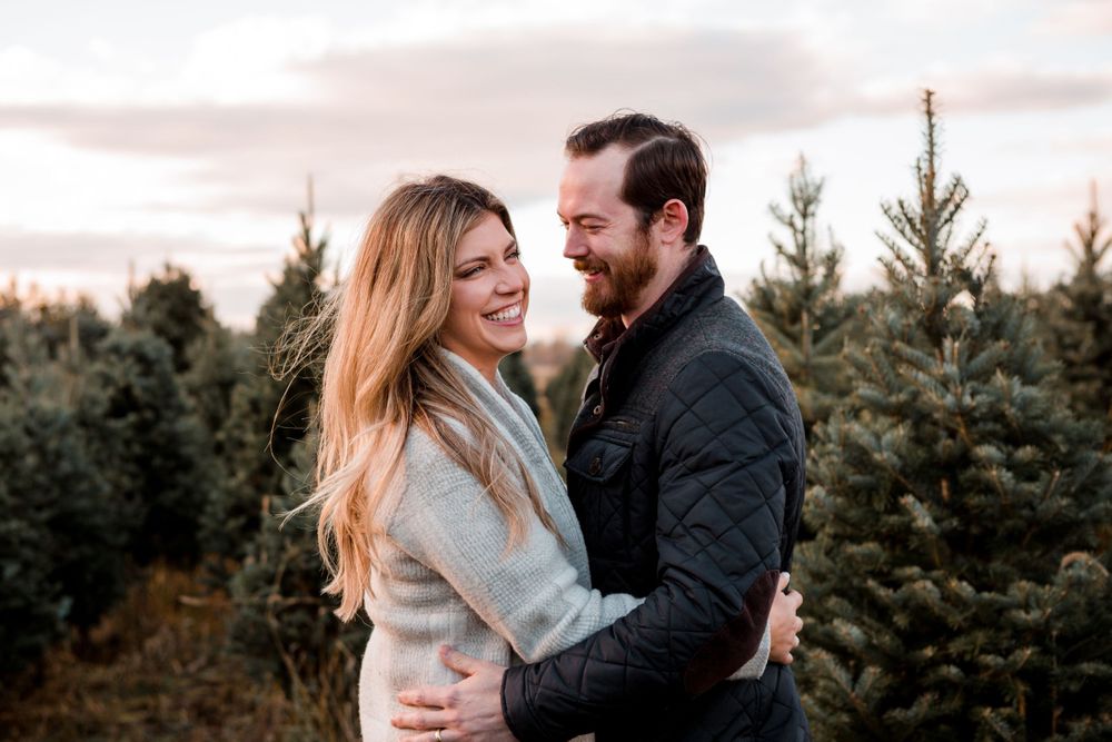 Couple embracing among evergreen trees at sunset.