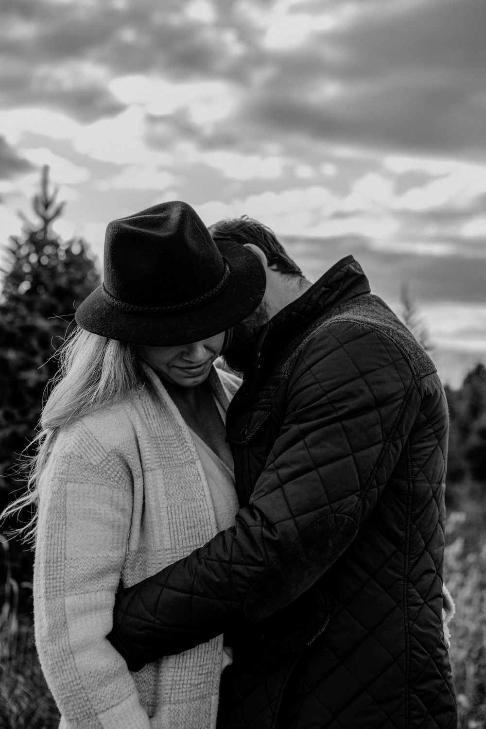 Romantic black and white portrait of couple in winter clothing among pine trees.