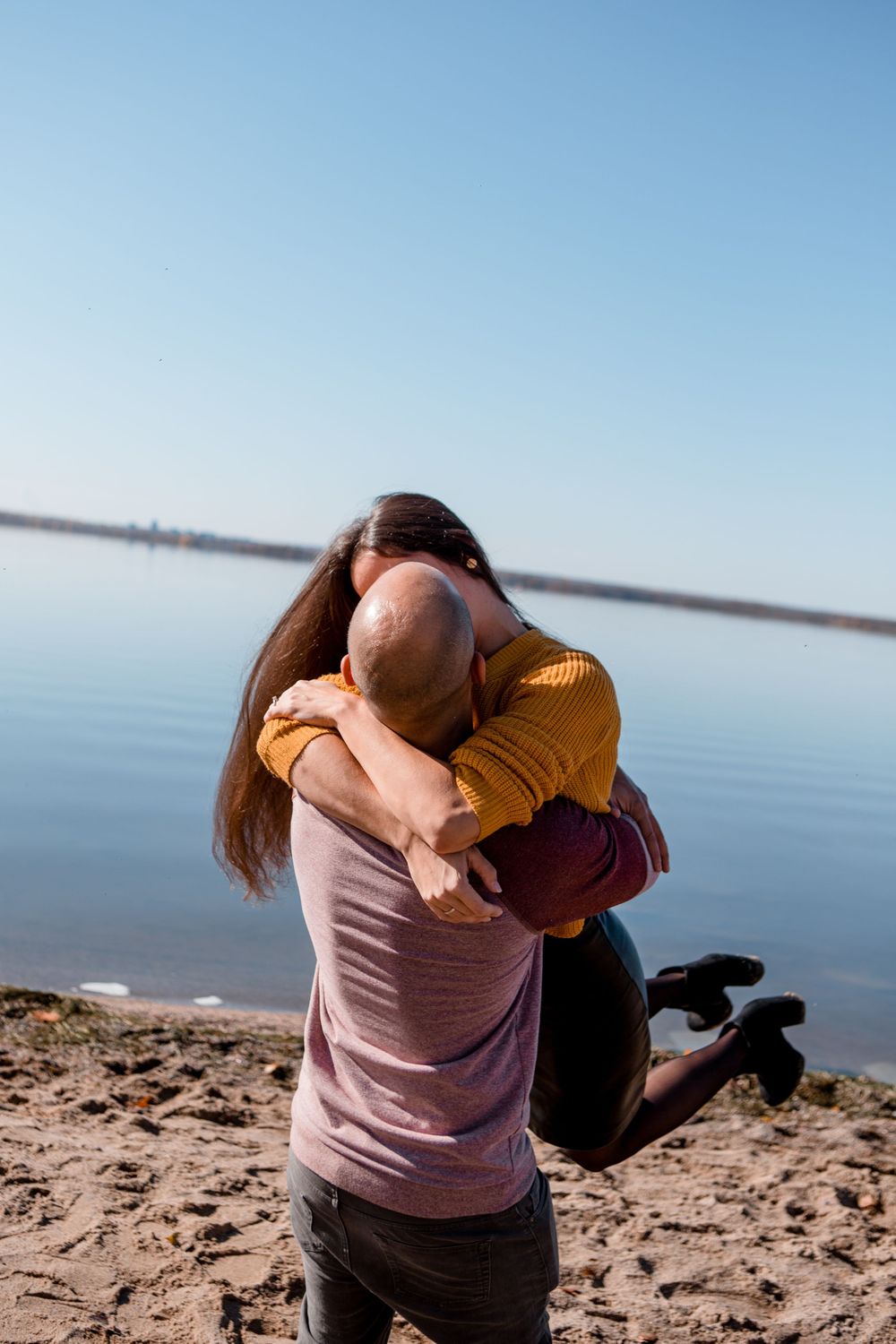 Couple embracing on sandy beach against calm blue water.