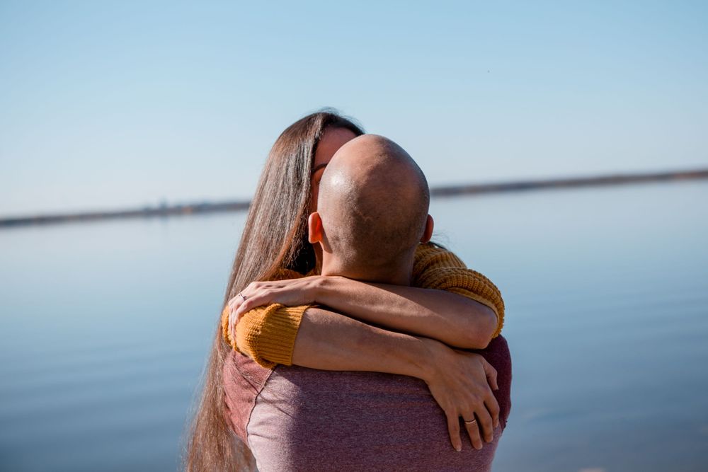 Couple in warm embrace looking out over serene lake on sunny day.