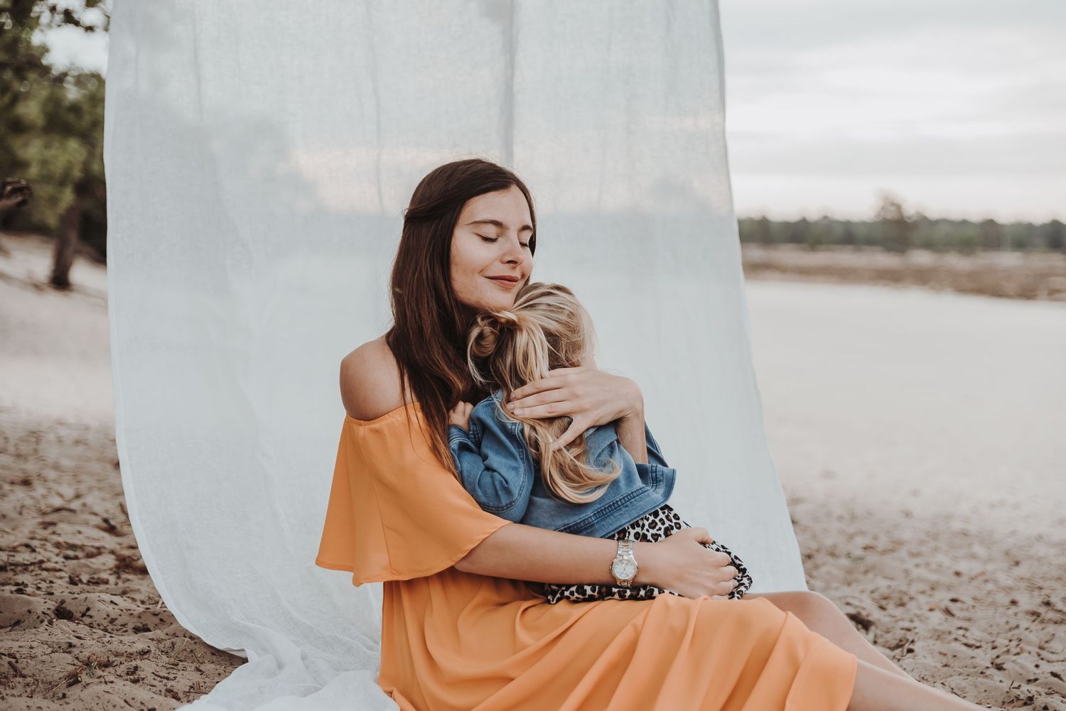 Woman in orange dress sits peacefully by the water with gentle expression.