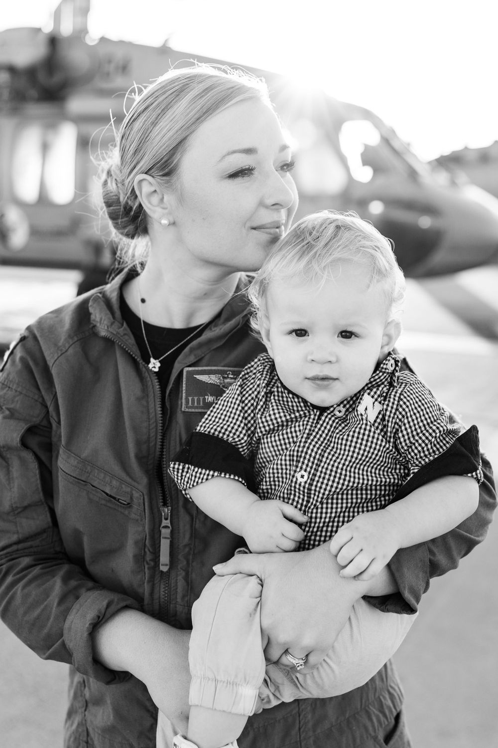 Military servicewoman in flight suit holding toddler in black and white portrait.