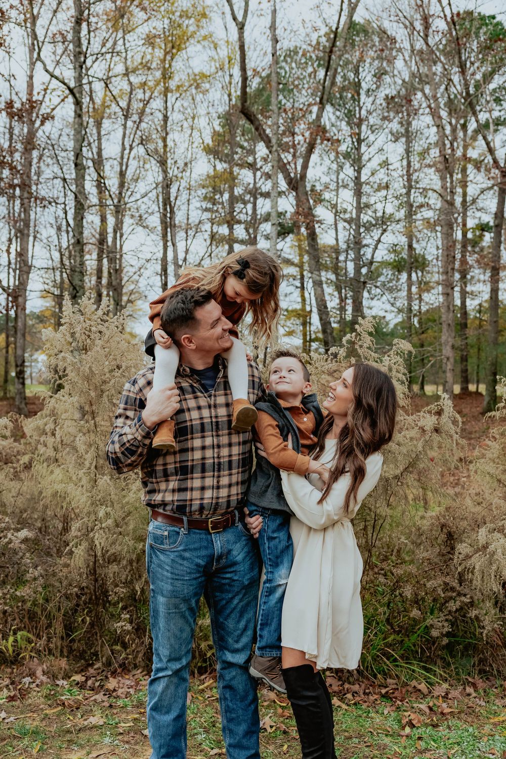 A couple shares tender moments outdoors among tall trees and autumn foliage.