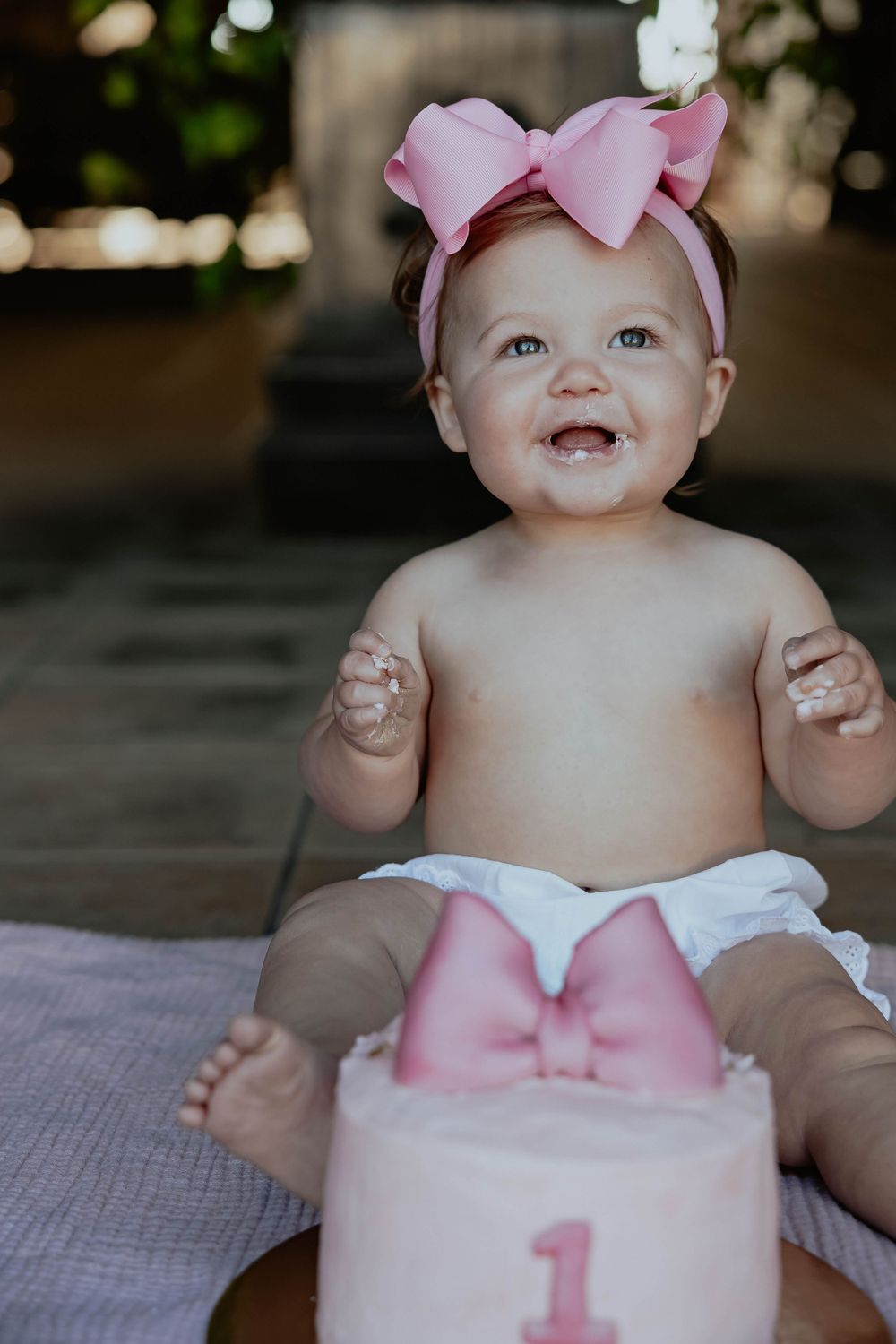 Baby wearing pink outfit and bow smiles during first birthday photoshoot.