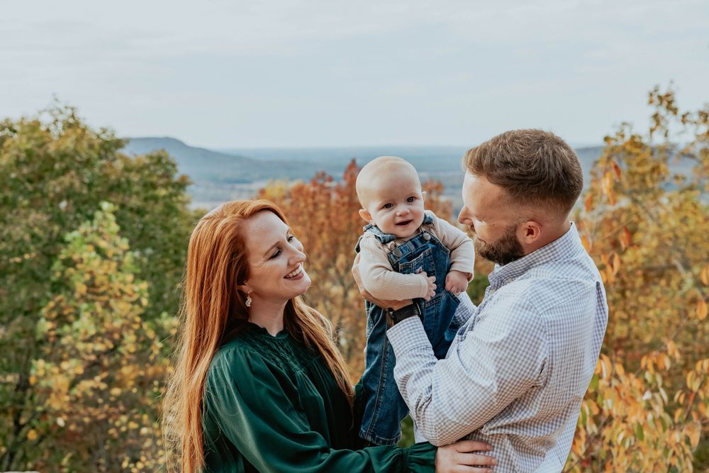 Family enjoying a playful autumn photoshoot outdoors with fall foliage in the background.