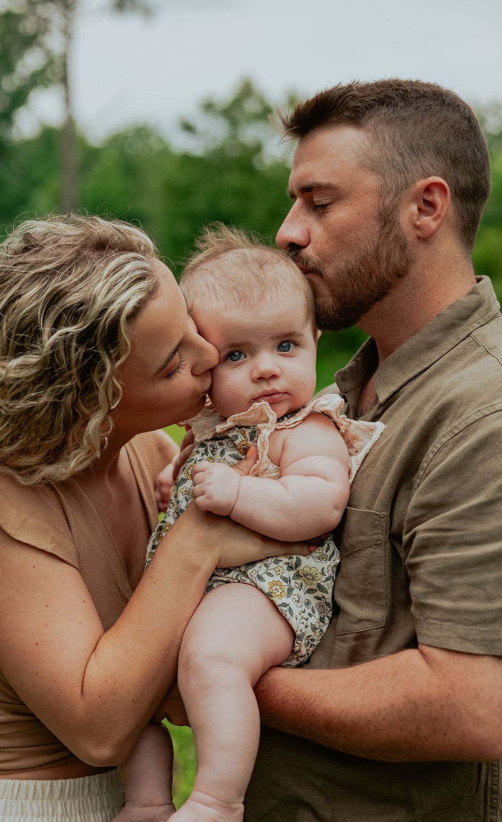 Sweet family moment captured outdoors with parents kissing their baby.