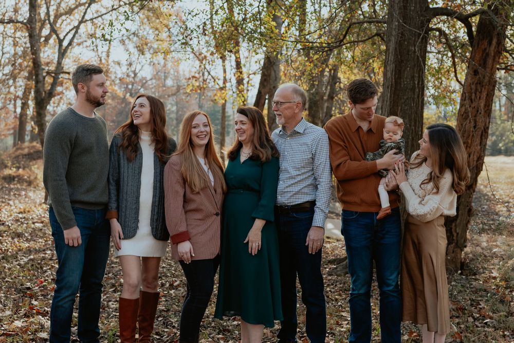 Large family group poses together for a casual outdoor photo among autumn trees.