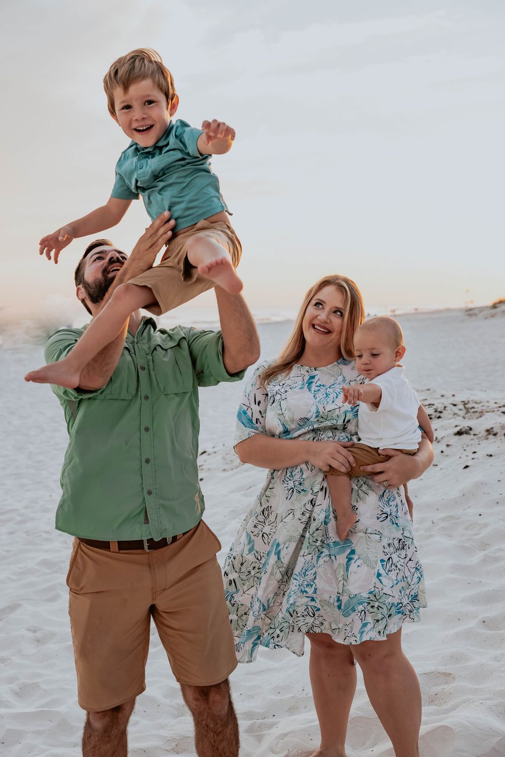 A family plays and laughs together on a sunny beach with white sand.