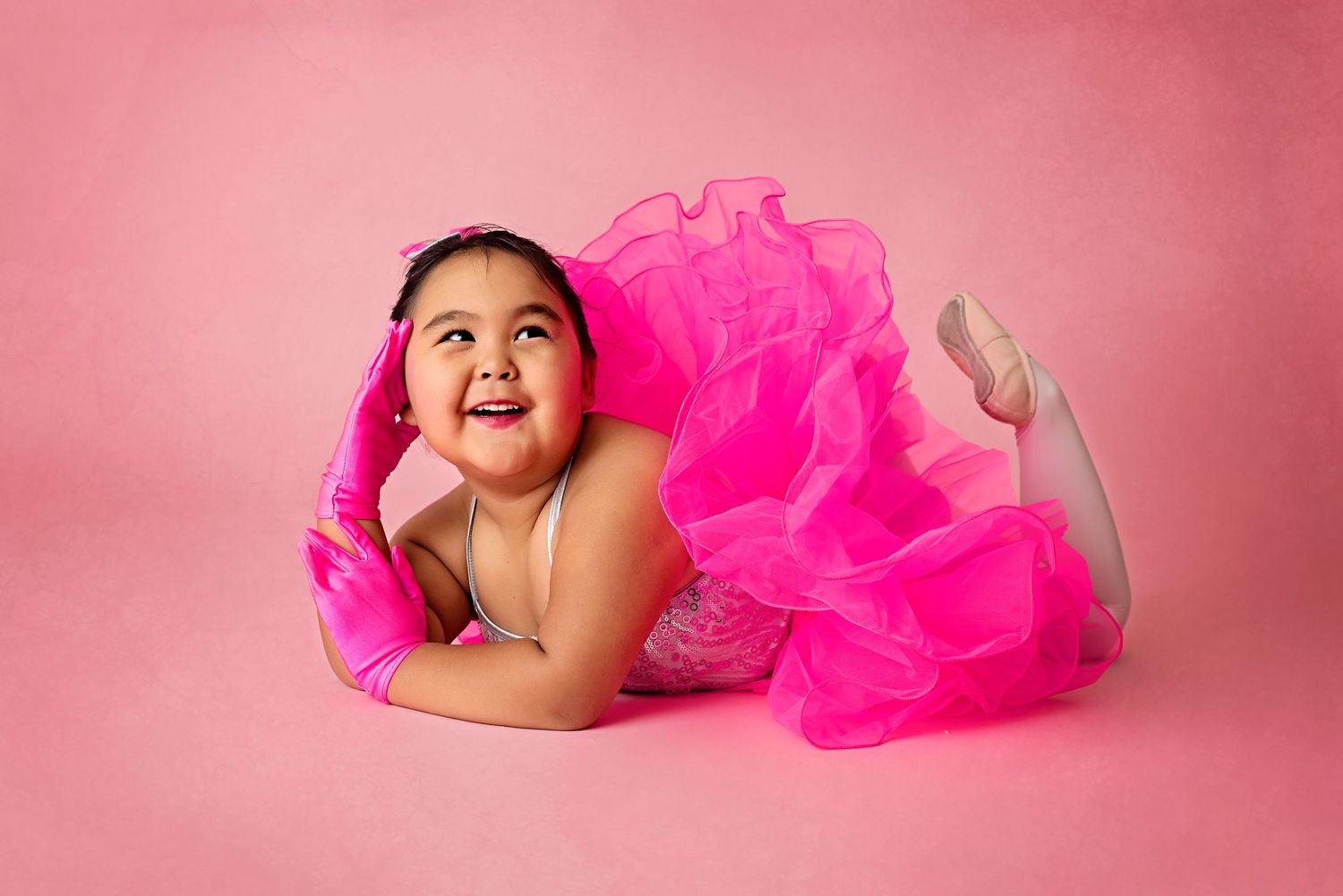 Joyful portrait with bright pink tulle dress against pink backdrop.