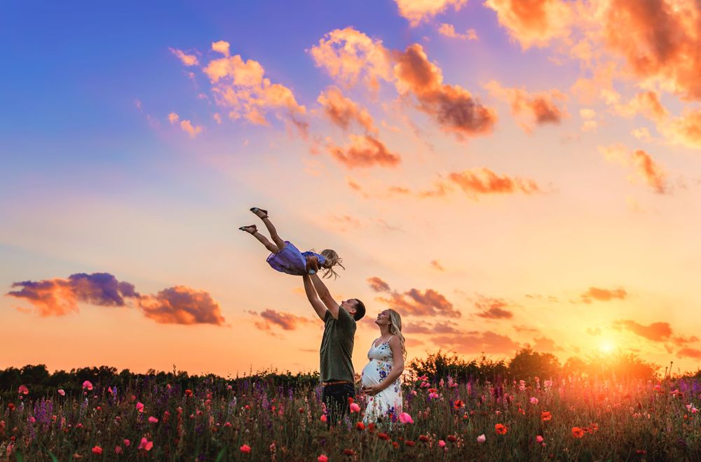 Silhouettes play in a flower field against a dramatic orange sunset sky.