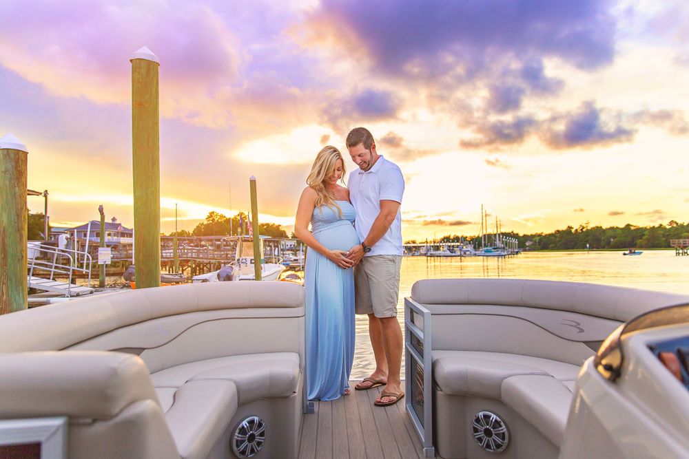 Couple stands on a boat deck against a colorful sunset harbor backdrop.