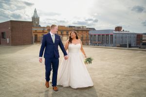 A couple walks hand in hand on a rooftop terrace with a city skyline in the background.