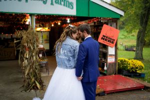 A couple shares an intimate moment outside a rustic farm stand with fall decorations.