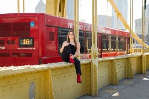 A dancer poses on a yellow bridge with a red streetcar in the background.