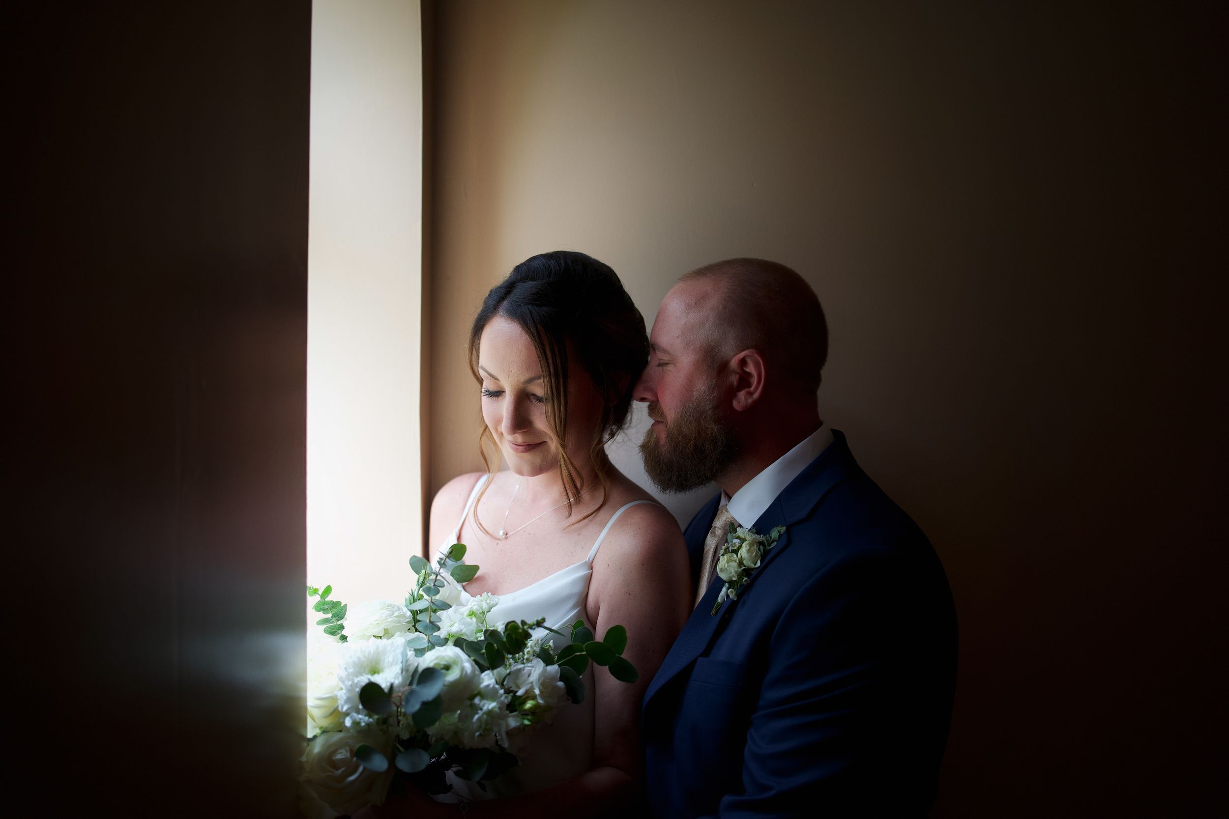 A dramatic window-lit portrait of a couple on their wedding day.