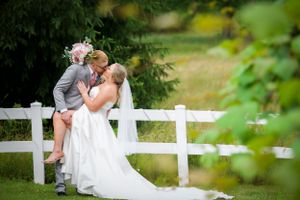 A tender moment between a couple in wedding attire by a white fence.