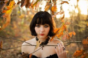 Autumn portrait in a black dress with orange leaves and soft bokeh lighting in the background.
