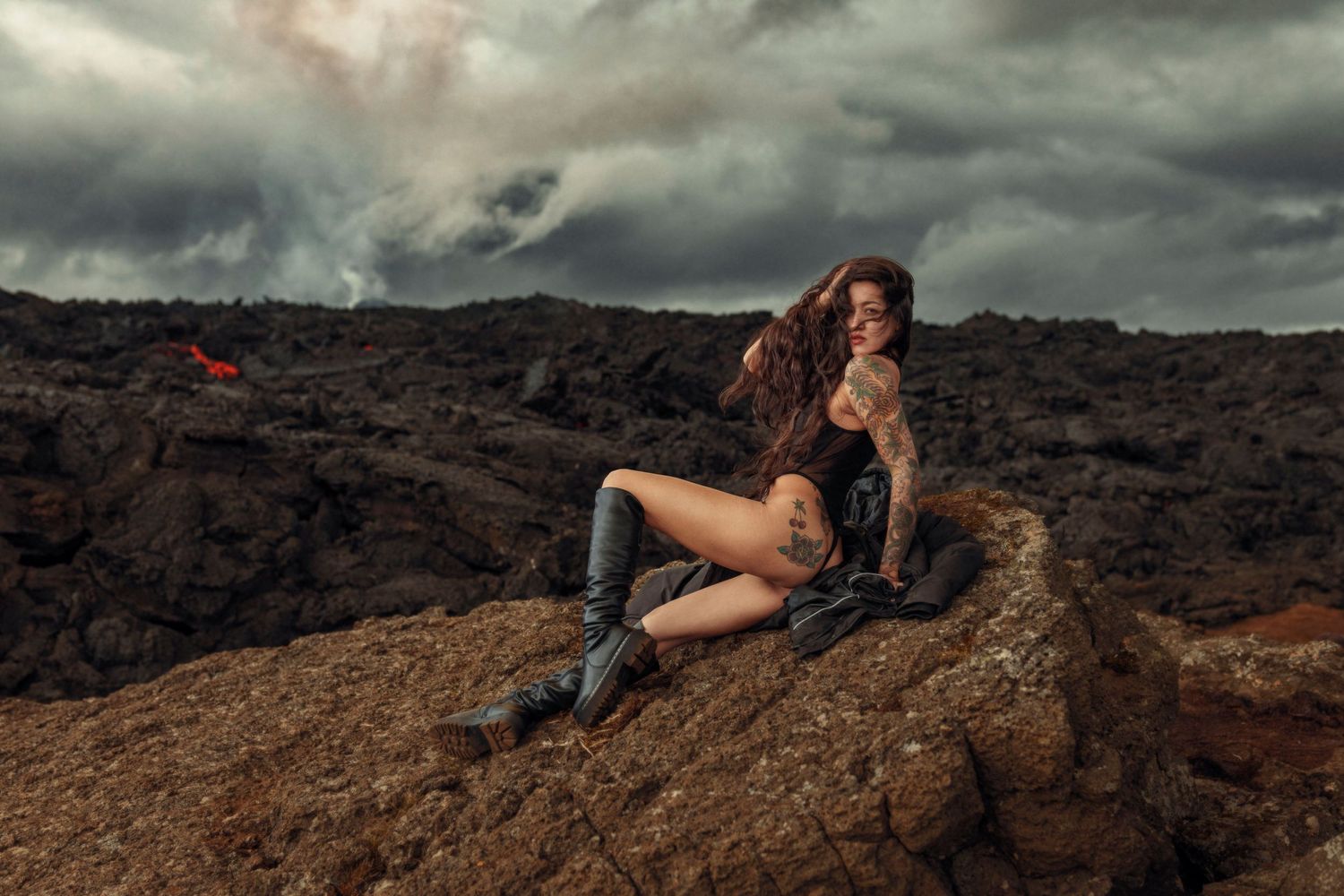 Moody fashion portrait on volcanic rocks under dramatic stormy sky.