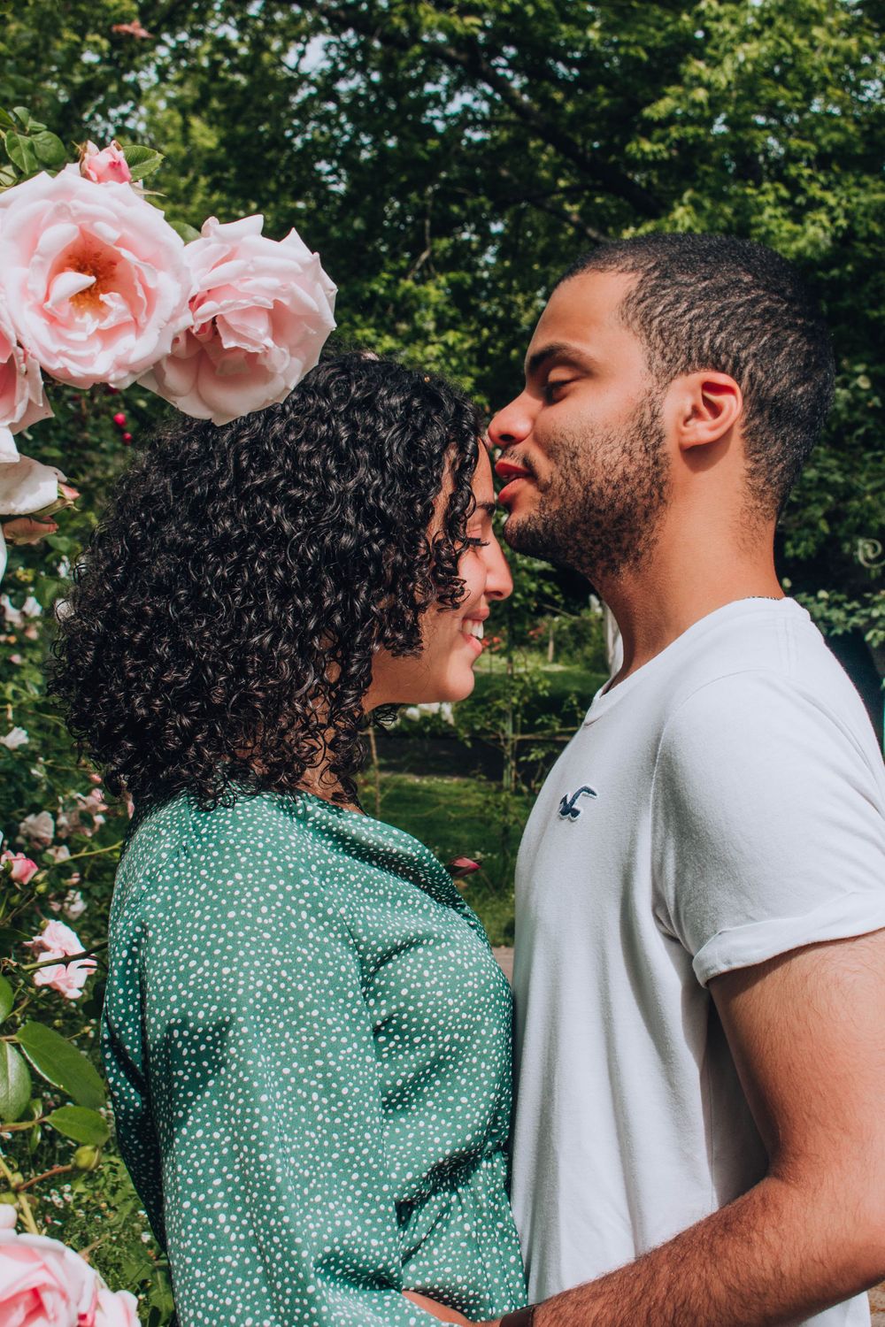 A romantic couple embracing near pink roses in a garden setting.