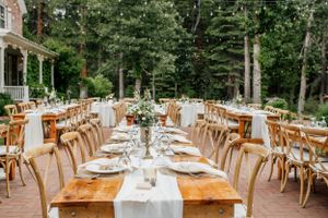 Rustic outdoor wedding reception tables set with white runners and wooden chairs.