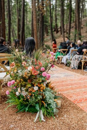 Beautiful floral arrangements with pink and orange blooms decorate a woodland wedding ceremony.