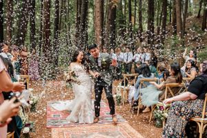 Confetti falls during a festive outdoor wedding ceremony in a forest setting.