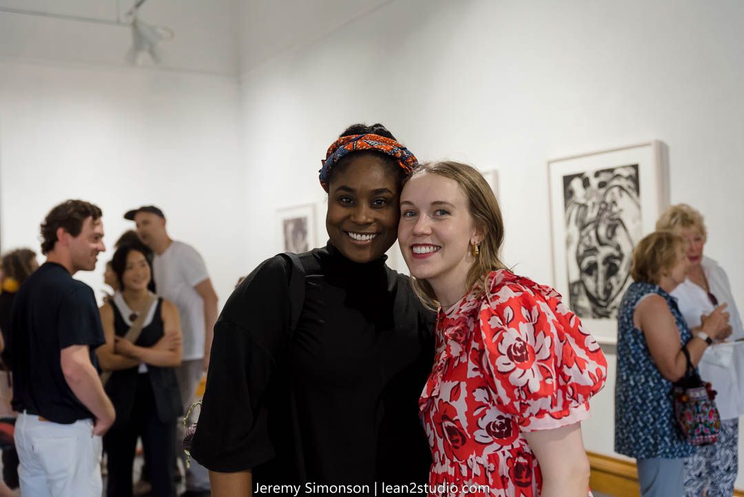 People gathered at an art gallery exhibition with framed artwork on white walls.