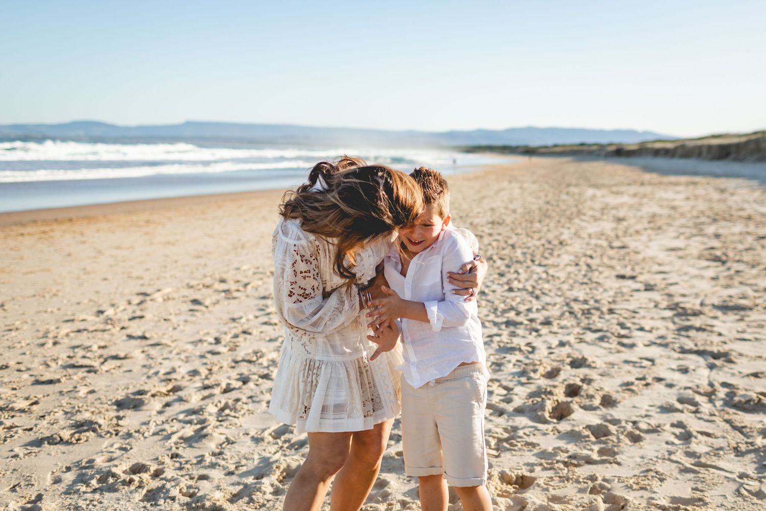 Joyful interaction between people on a sandy beach with ocean waves in background.