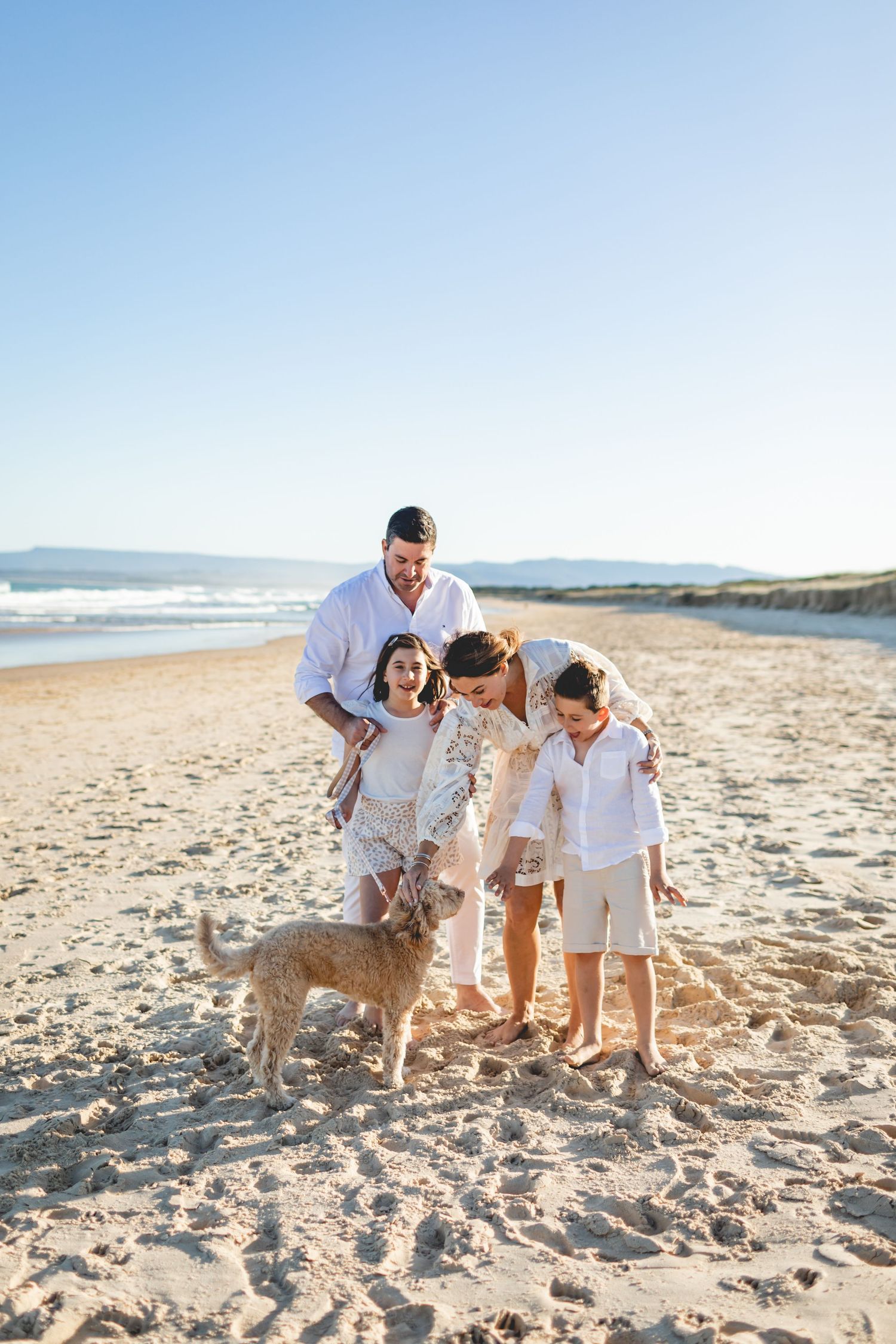 Group playing with their dog on sandy beach during sunset.