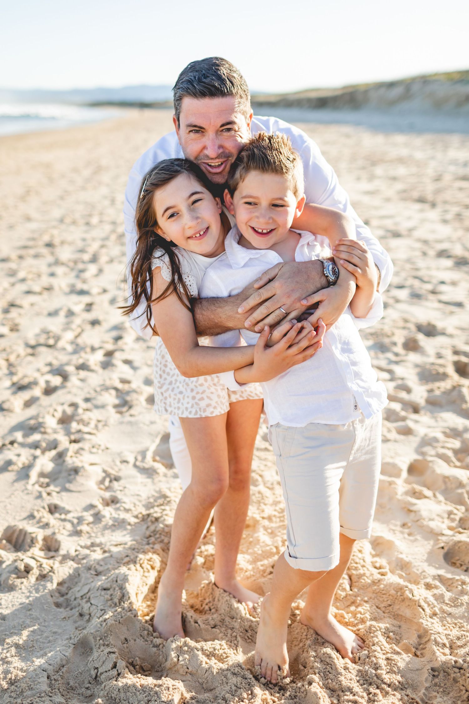 A family shares joyful hugs and laughter while playing together on a sunny beach.