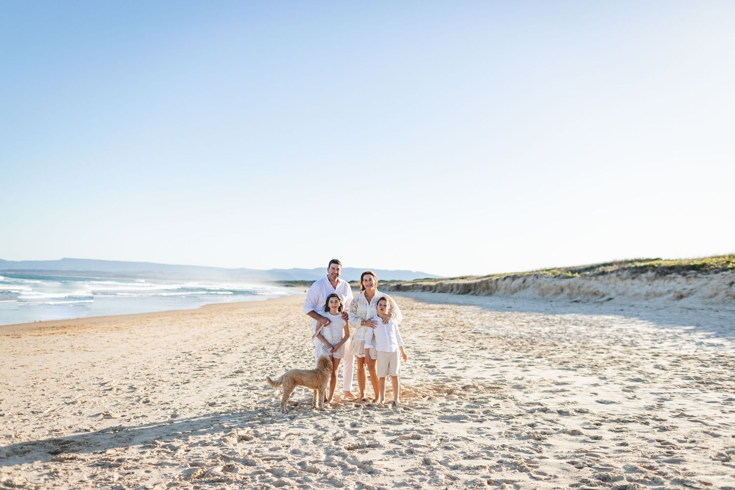 Group standing together on sandy beach with ocean waves in background.