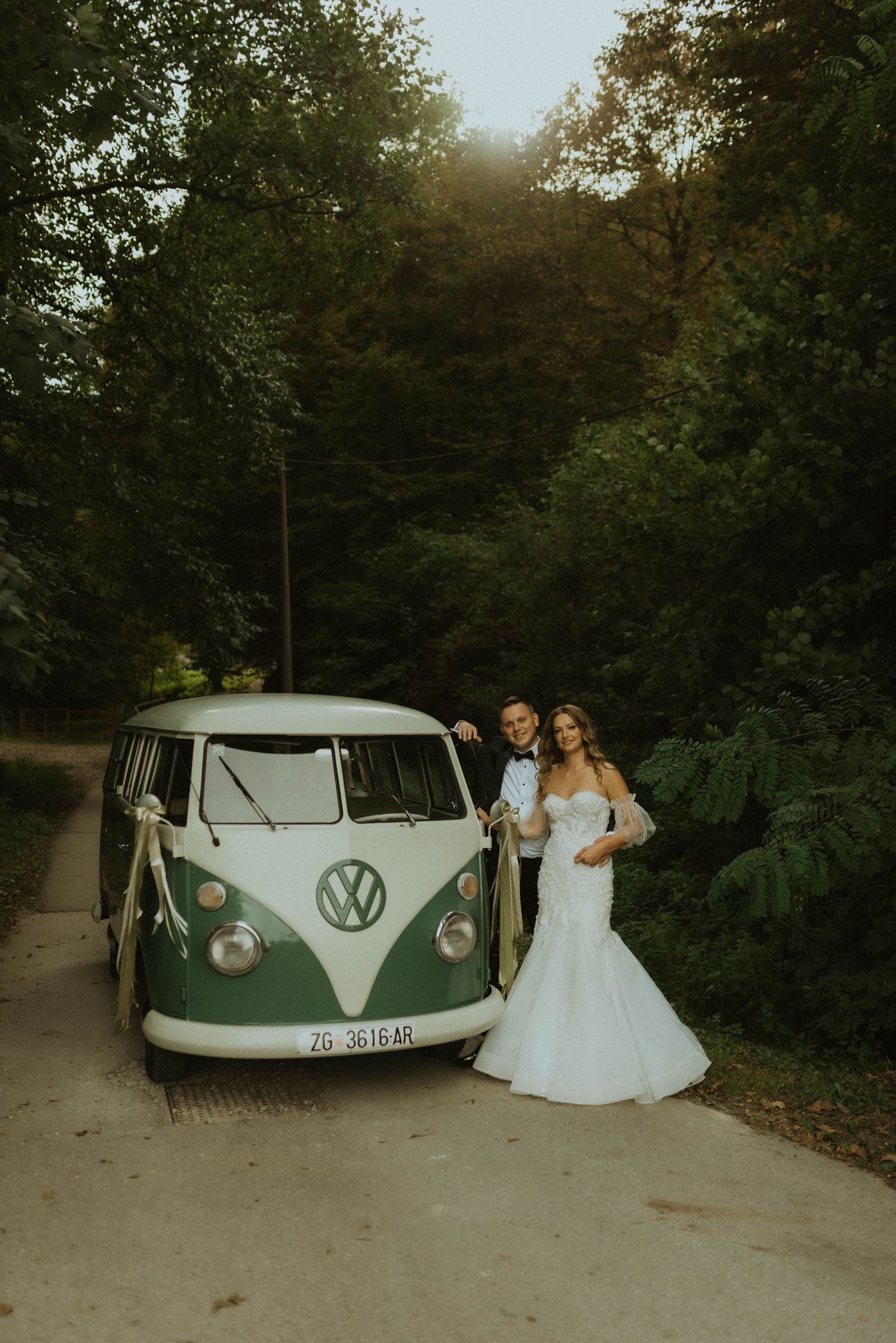 Vintage green VW bus with wedding couple in romantic forest setting.