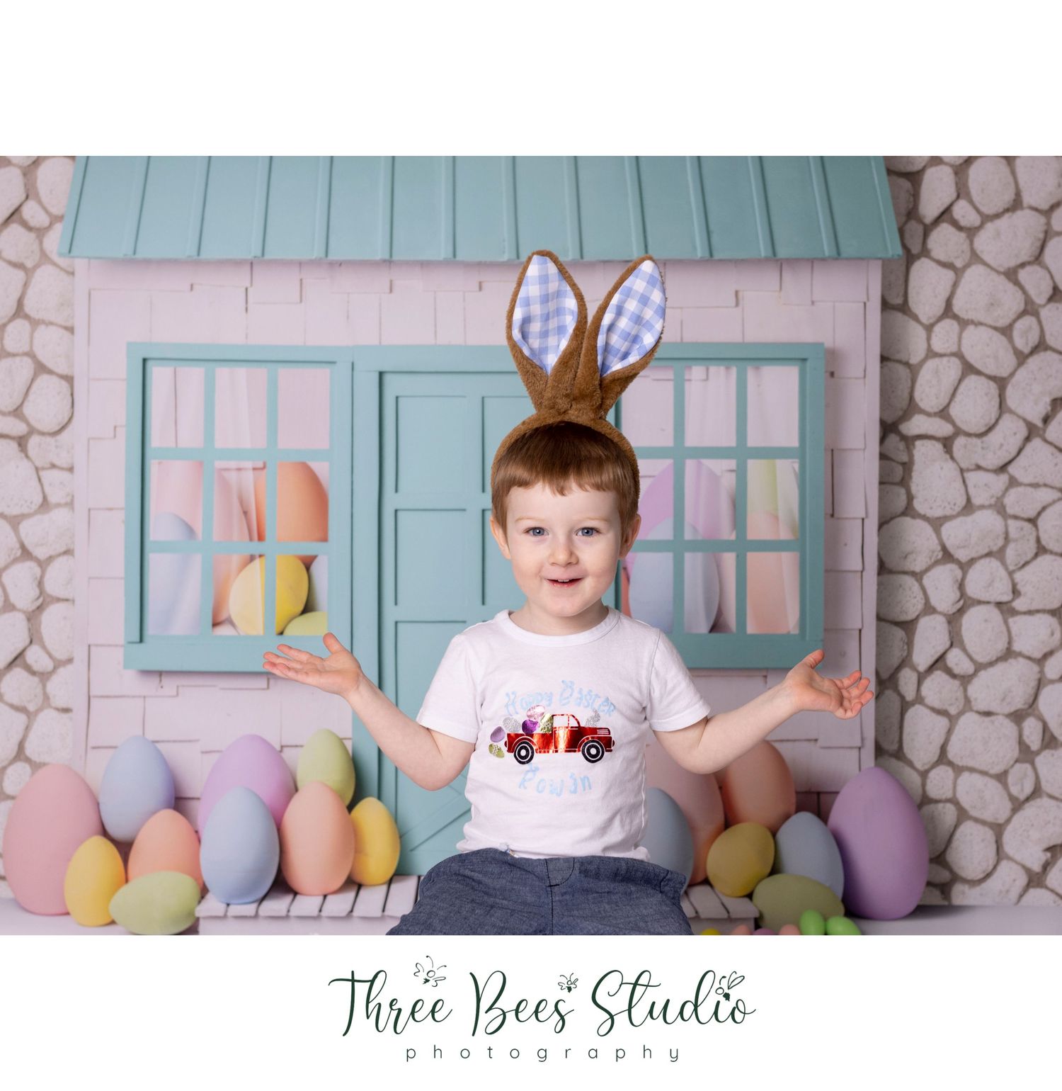 Easter themed photo setup with pastel eggs and bunny ears against blue house backdrop.