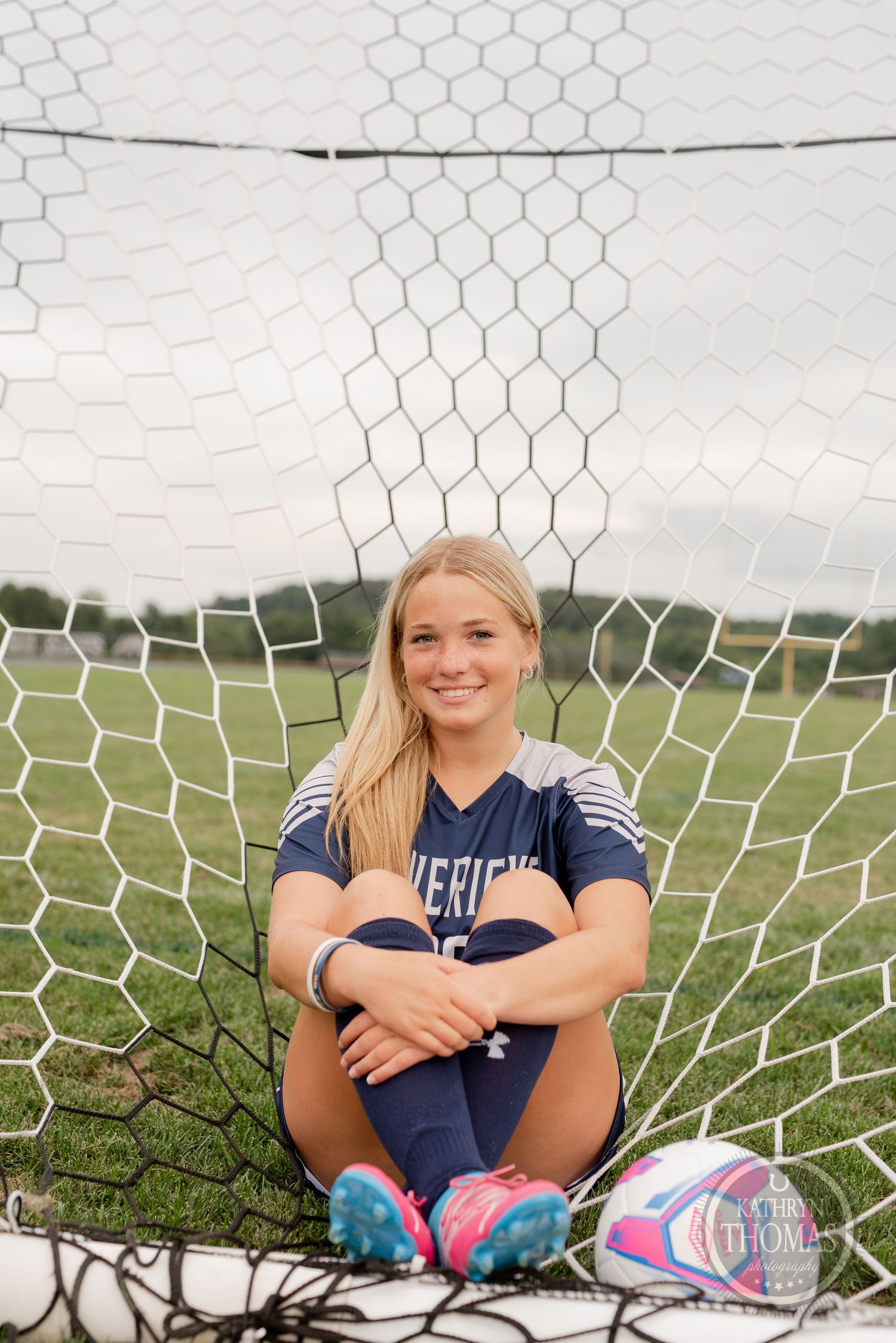 Soccer player sits in goal net wearing navy Mavericks jersey number 20 and colorful cleats.