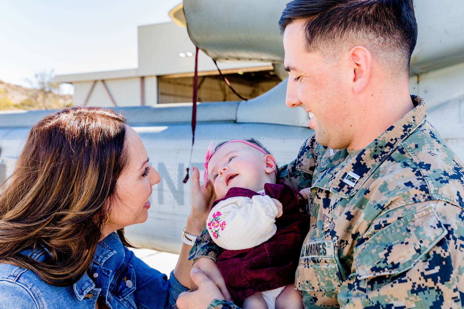 Military homecoming moment with baby at aircraft hangar.