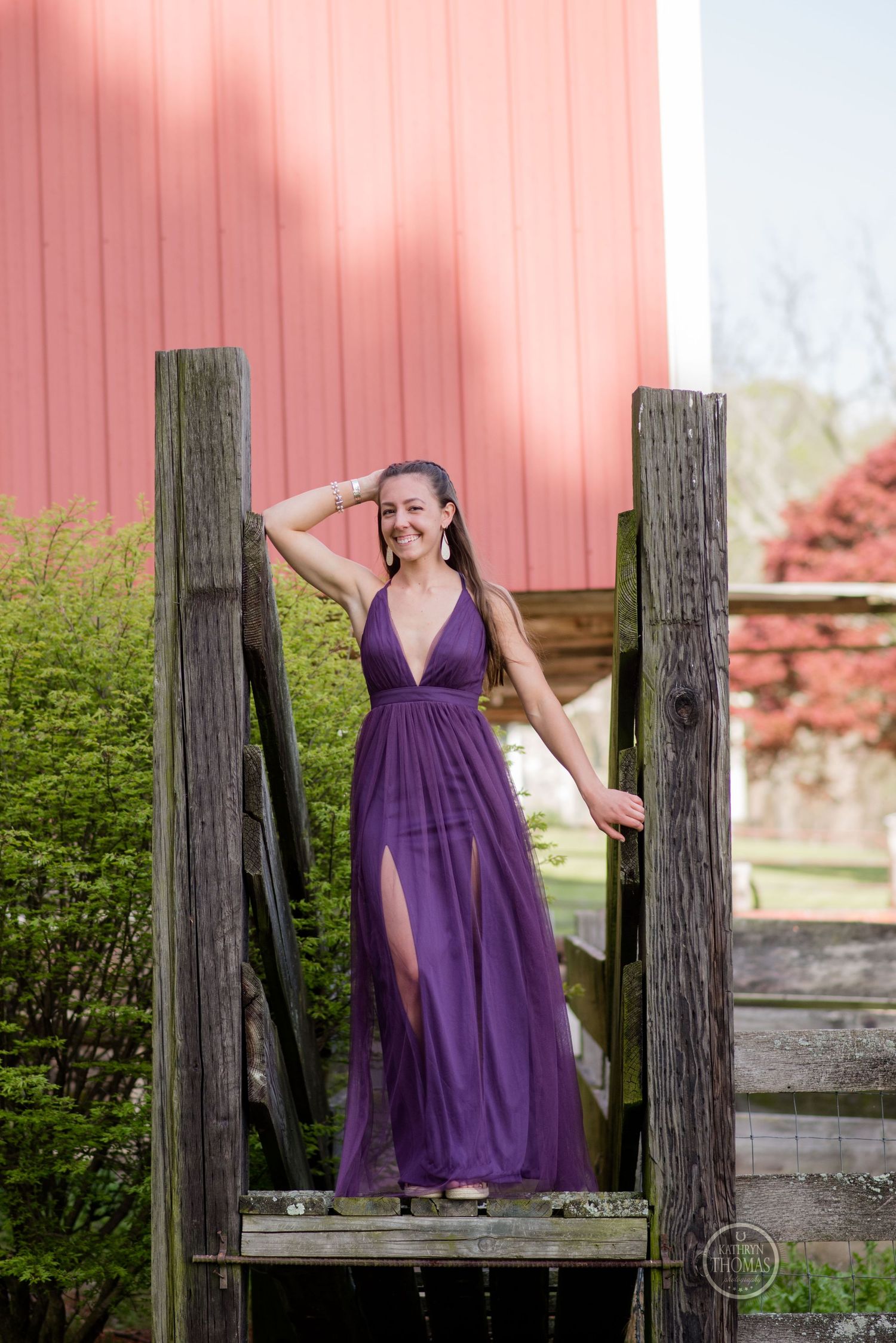A flowing purple gown contrasts against a pink barn wall and rustic wooden posts.