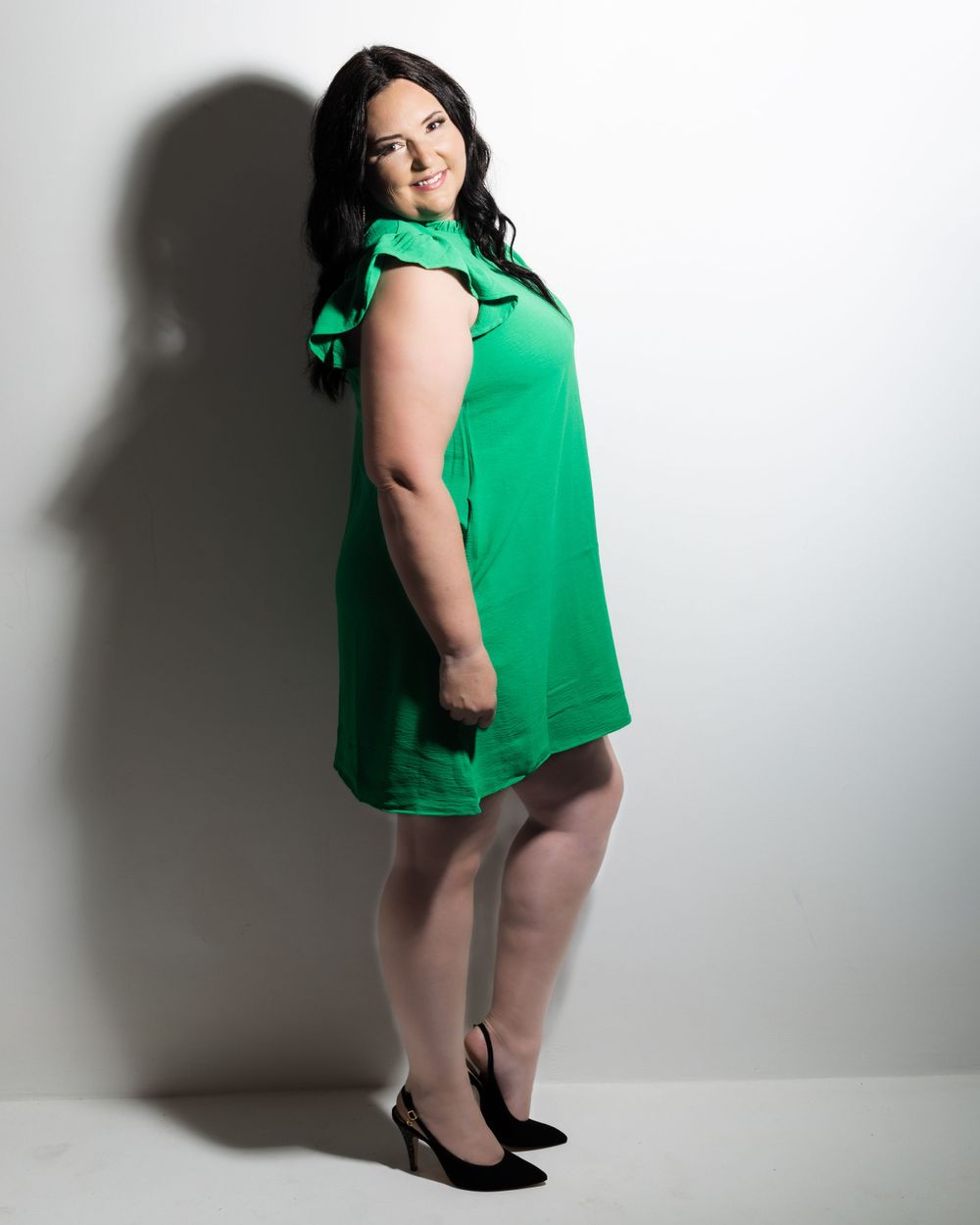 middle aged female in a green dress posing and smiling against a white wall