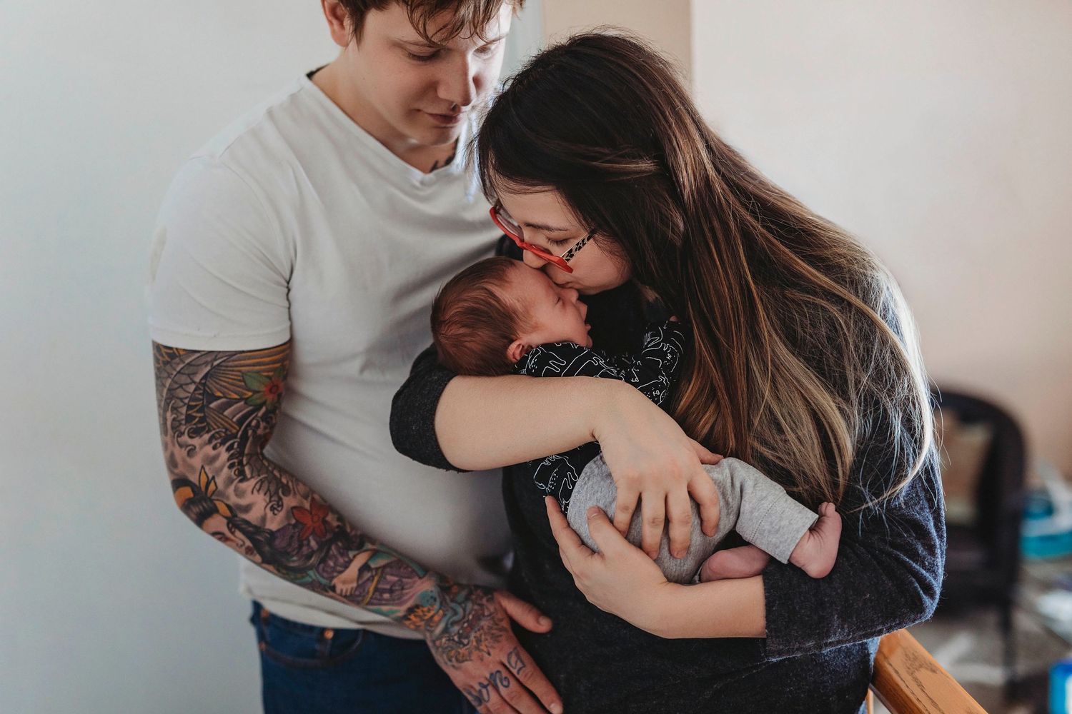 Family sharing intimate moment with newborn baby in casual home setting.