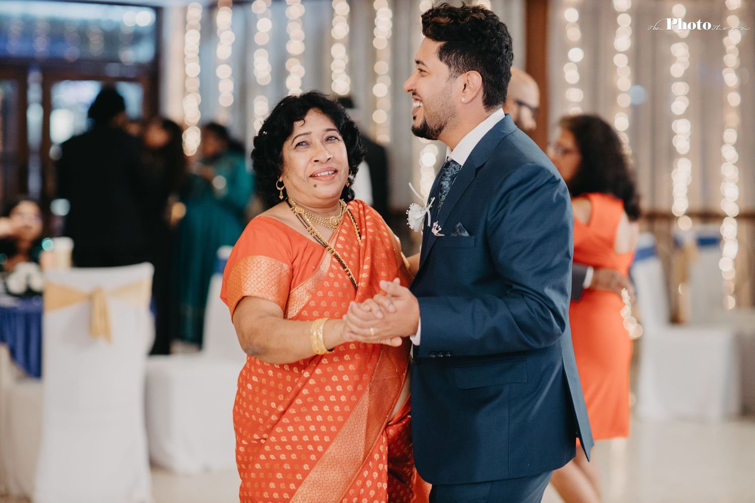 Wedding guests in bright orange attire dance during reception celebration.