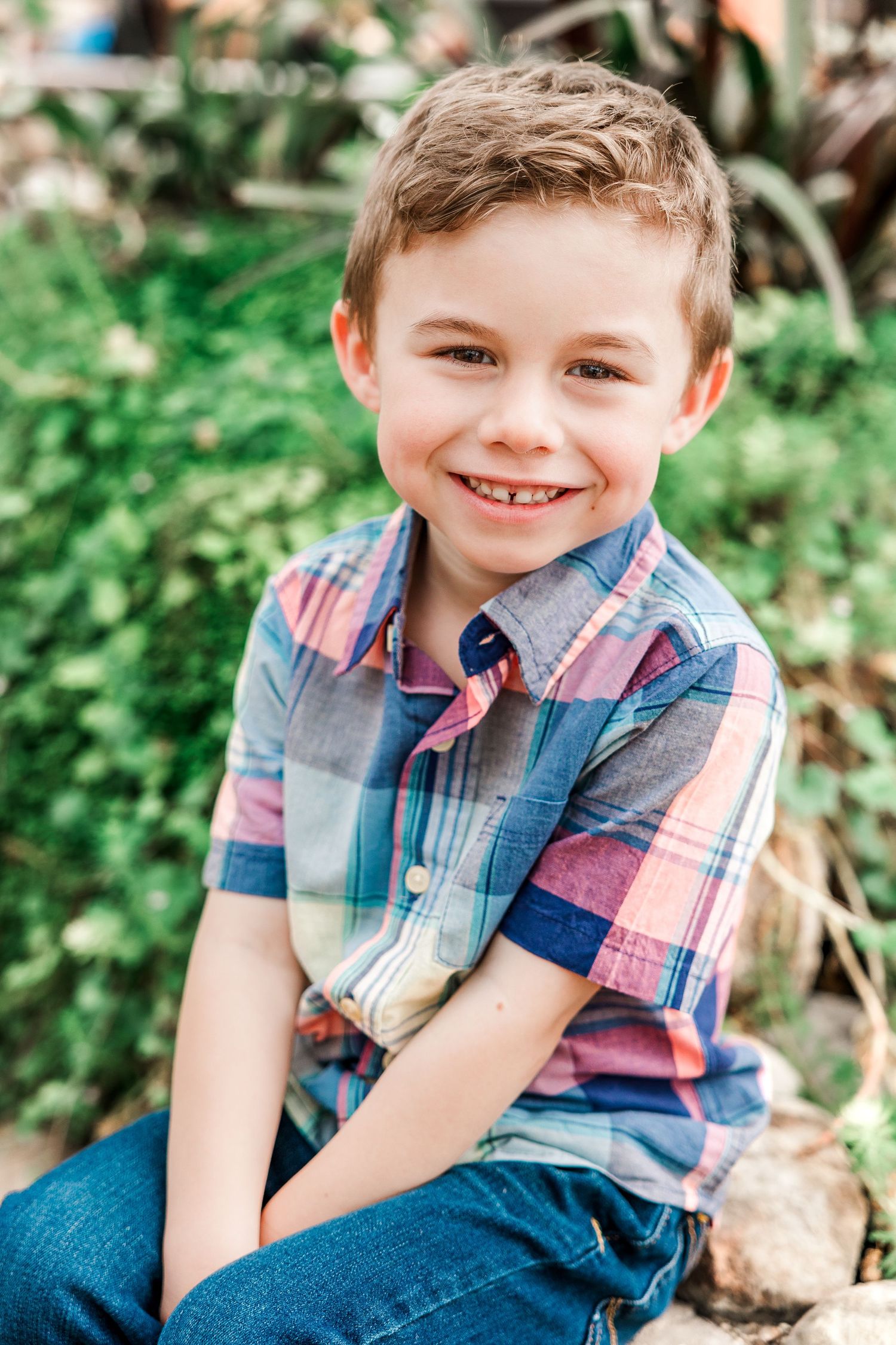 A casual portrait in a plaid shirt against leafy green foliage.