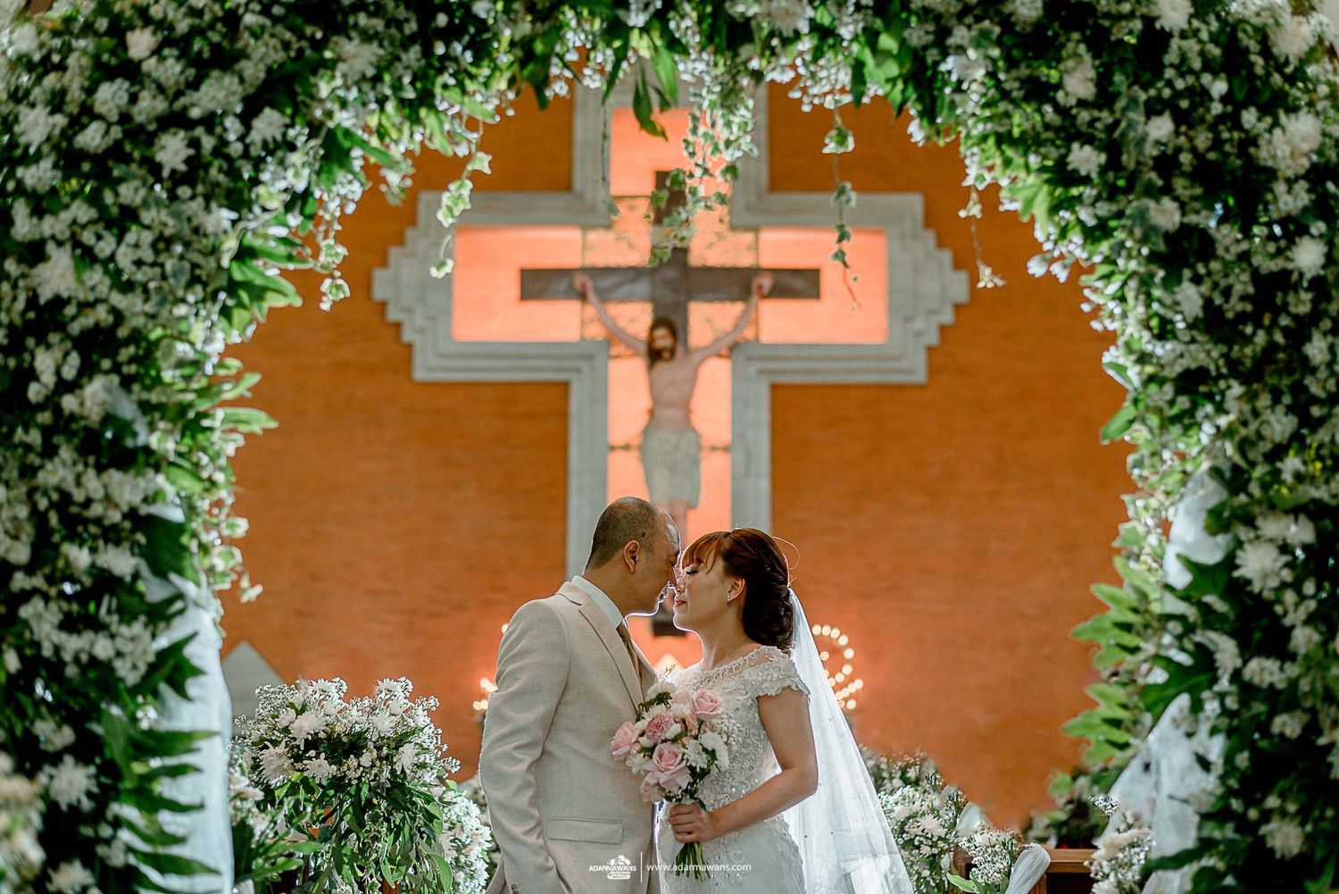 Wedding ceremony setup with cross and floral arch decorated with white flowers.