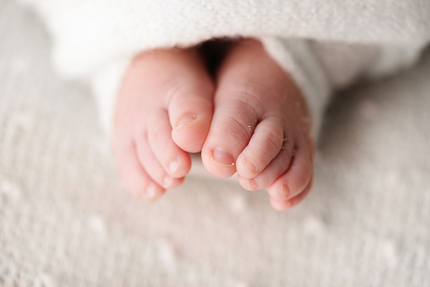 Close-up of tiny newborn feet peeking out from white blanket.