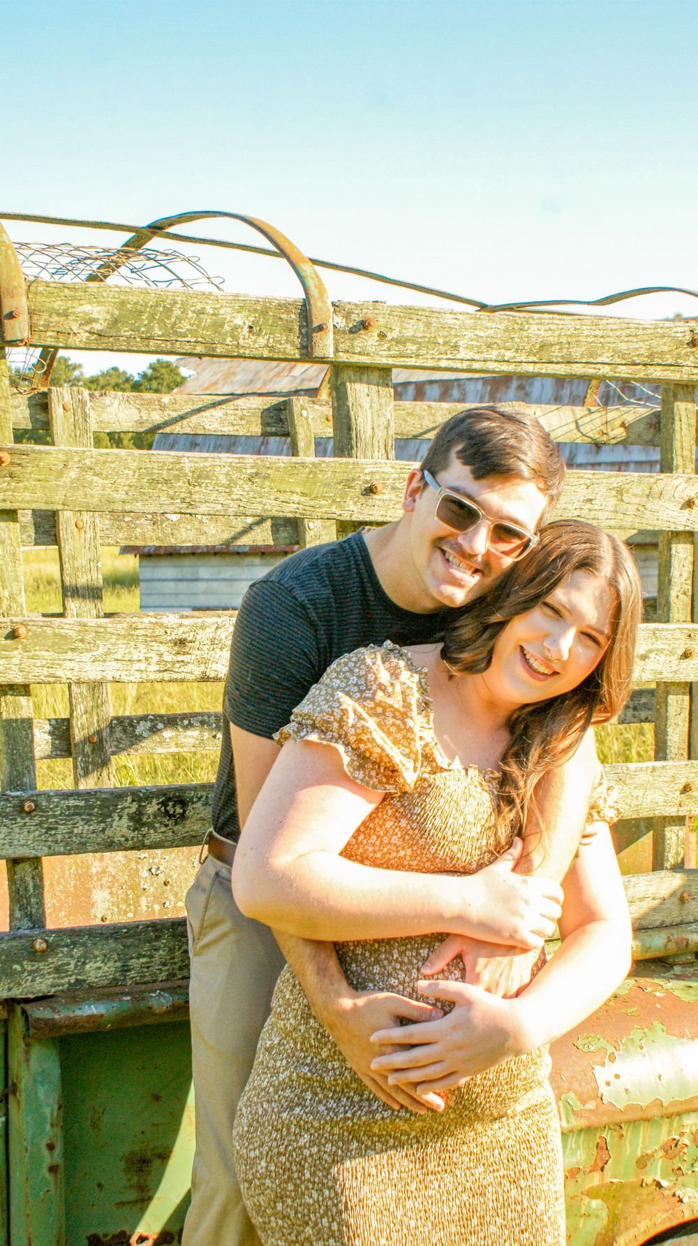 A maternity photoshoot by a rustic wooden fence during golden hour.